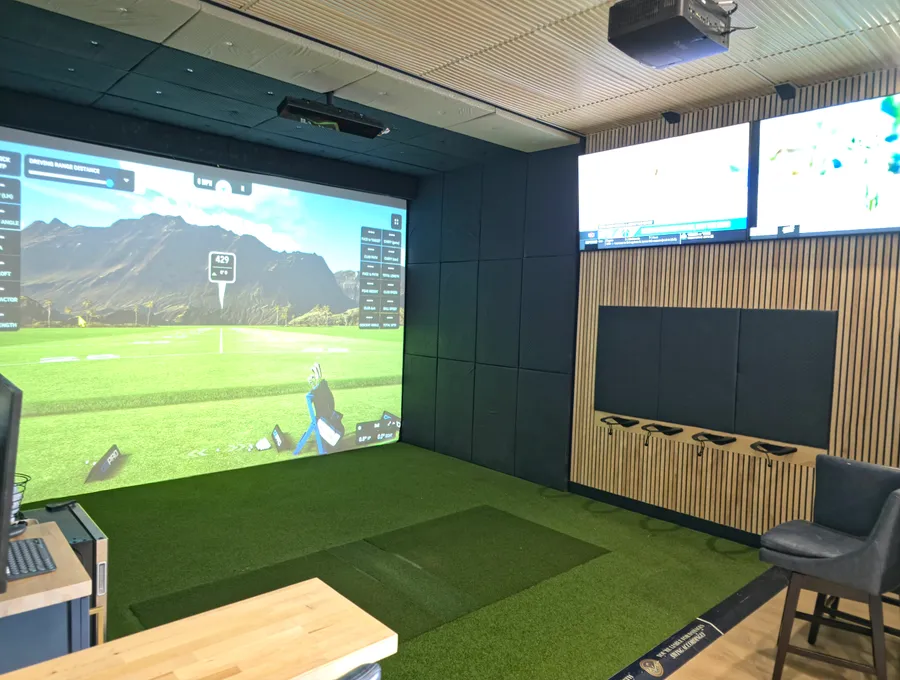 Golf simulator bay at the All Seasons showroom with impact screen, turf, and live shot data