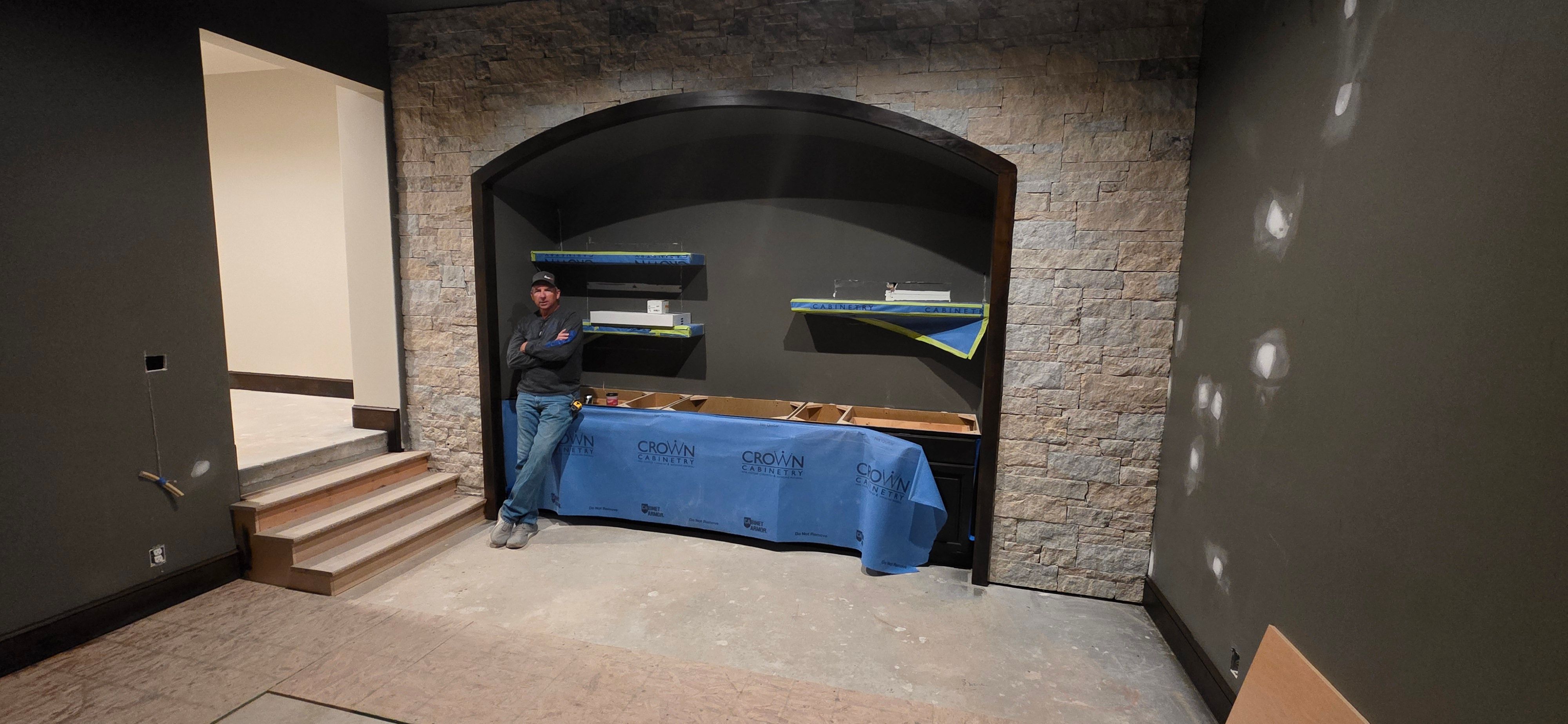 Custom built-in cabinetry under a stone arch beside the Grain Valley golf simulator bay