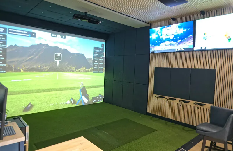 Golf simulator room with wood-slat walls, putting turf, and a course on the impact screen in Kansas City