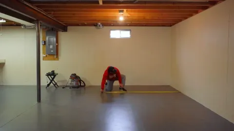 Measuring an empty basement with a tape measure to design a golf simulator room
