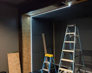 Golf simulator enclosure roughed in with an LED-lit screen opening and acoustic panels