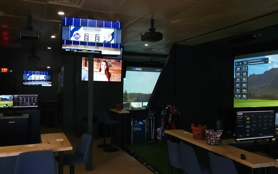 Finished multi-bay golf simulator lounge with screens, TVs, and bar seating