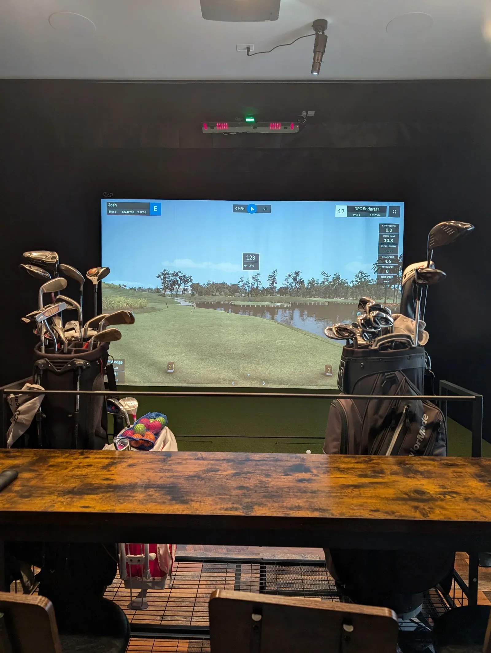 Finished home golf simulator bay with a course on screen, golf bags, and theater seating