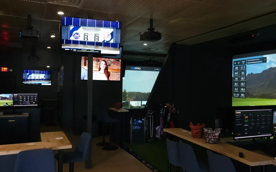 Finished multi-bay golf simulator lounge with screens, TVs, and bar seating